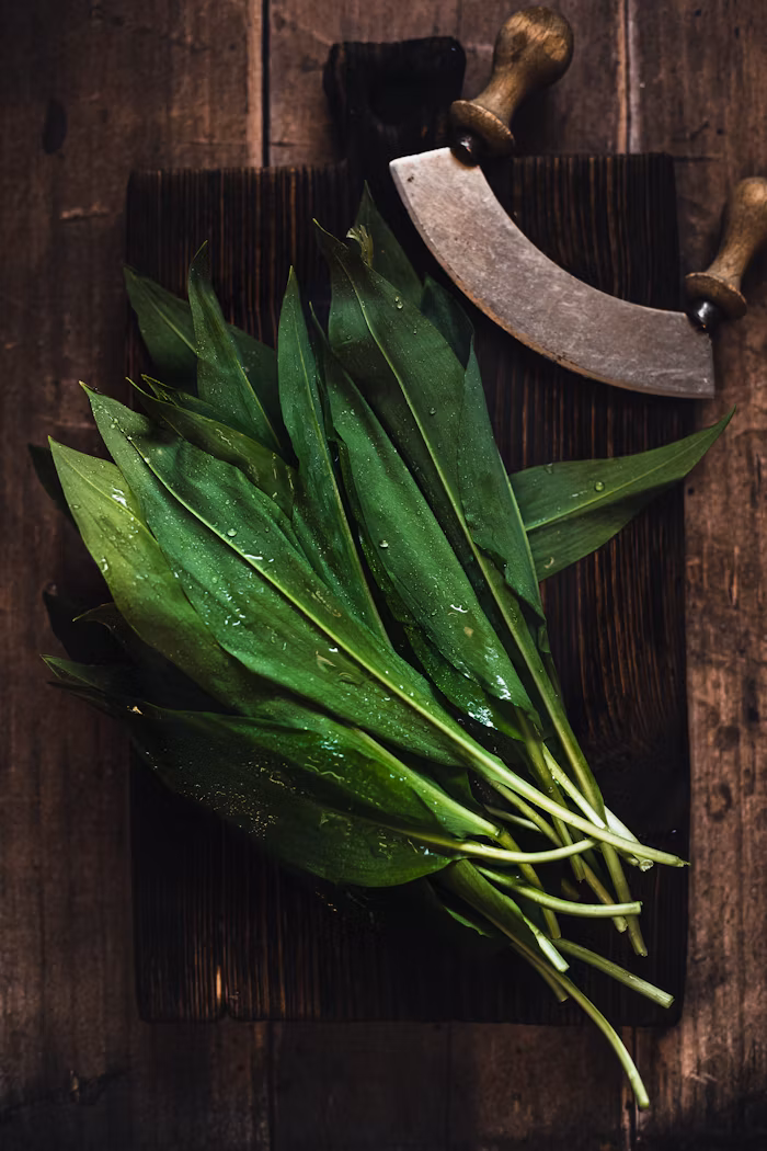 A bunch of fresh wild garlic waiting to be cut of a rustic chopping board