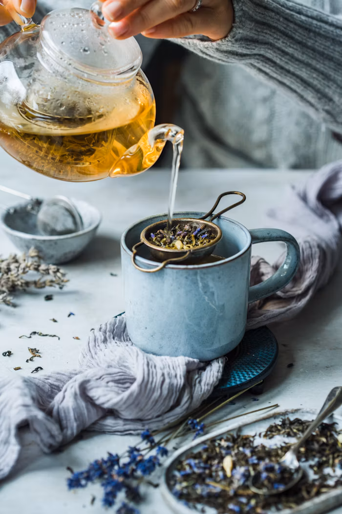 Hands pouring a pot of herbal tea into a cup through a strainer