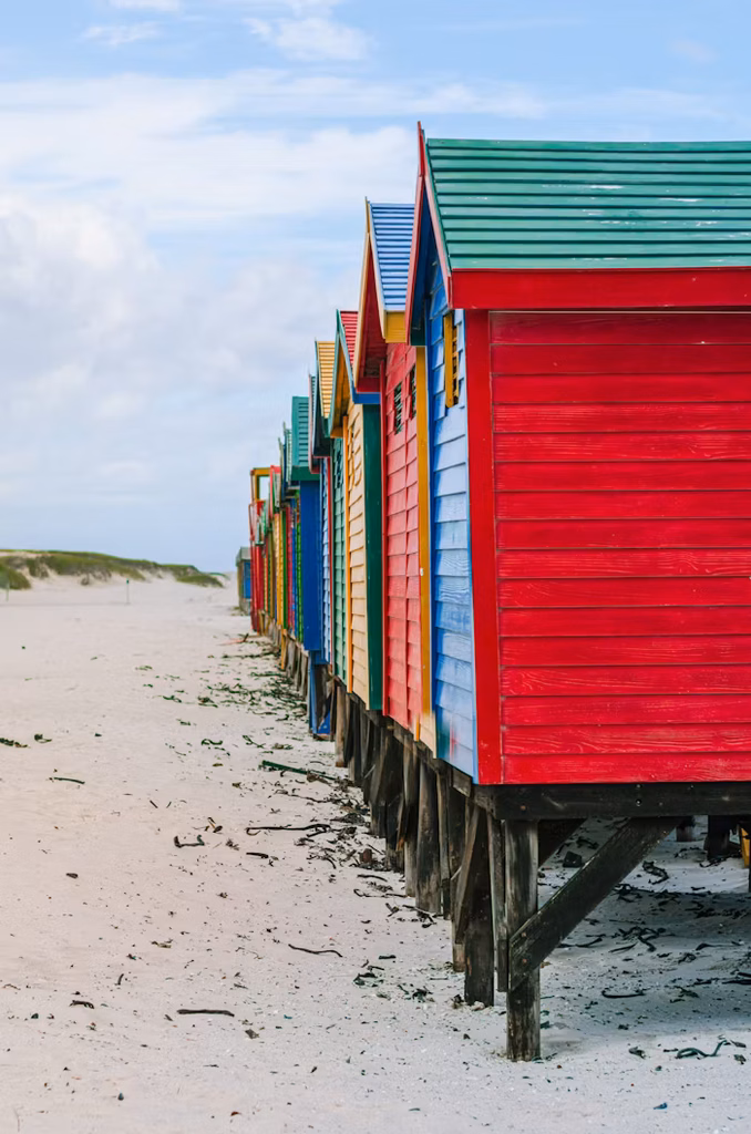 A row of brightly coloured beach huts standing on golden sands